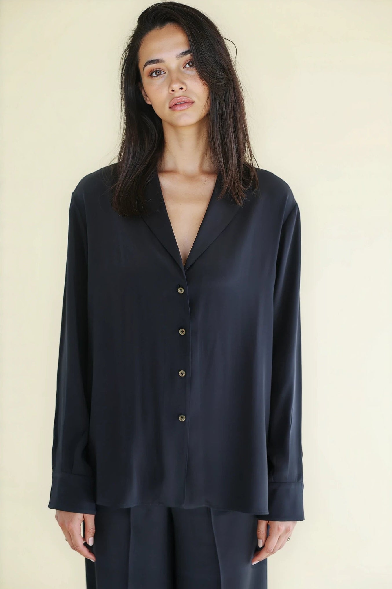 Woman wearing a navy silk satin pajama set against a plain background