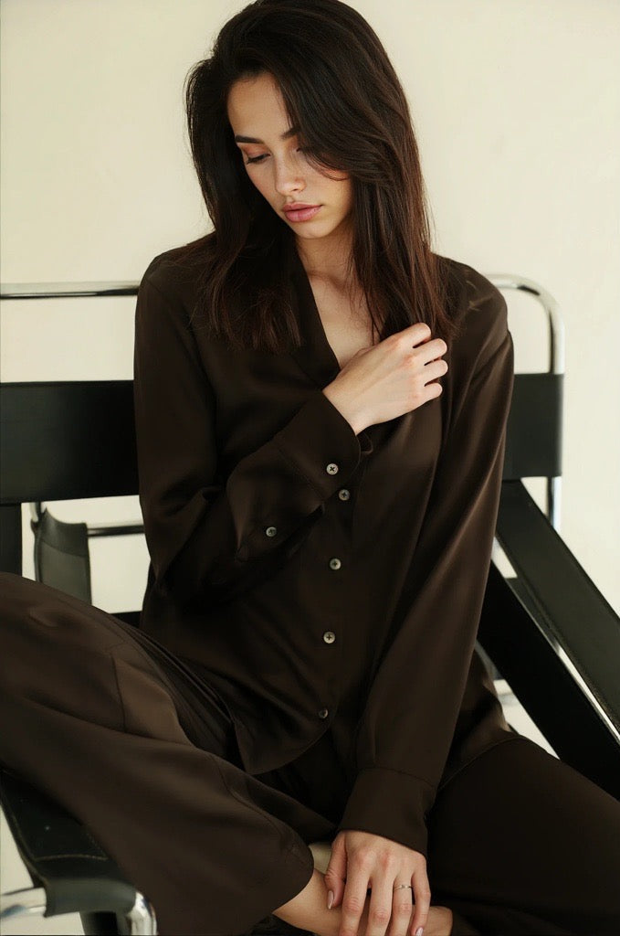 Woman wearing a brown outfit sitting on a chair against a white background