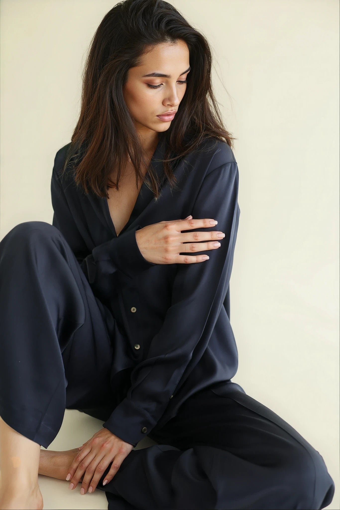Woman wearing a dark blue pajama set sitting on a white surface.